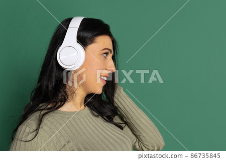 Profile view. Happy young beautiful girl with long glossy dark hair listening to music isolated on green background. Concept of emotions, facial expression Profile view. Happy young beautiful girl with long glossy dark hair listening to music isolated on green background. Concept of emotions, facial expression 86735845