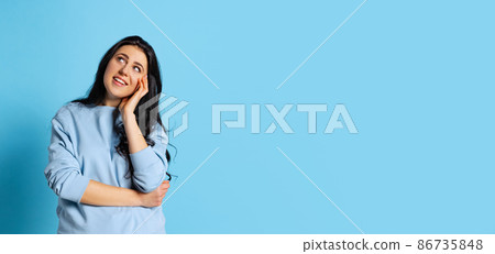 Portrait of young beautiful girl with long glossy dark hair posing isolated on blue background. Concept of emotions, facial expression Portrait of young beautiful girl with long glossy dark hair posing isolated on blue background. Concept of emotions, facial expression 86735848