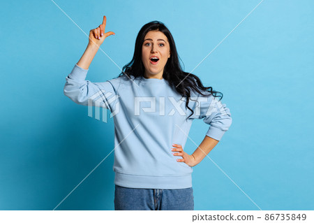 Idea, imagination. Portrait of young beautiful girl with long glossy dark hair posing isolated on blue background. Concept of emotions, facial expression Idea, imagination. Portrait of young beautiful girl with long glossy dark hair posing isolated on blue background. Concept of emotions, facial expression 86735849