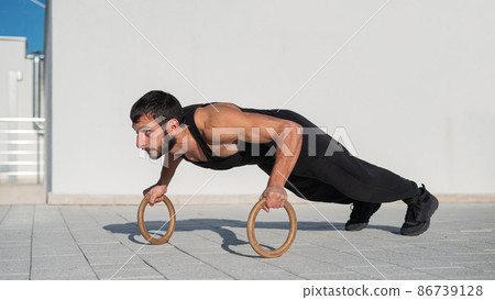 A man in black sportswear doing ring push-ups outdoors. A man in black sportswear doing ring push-ups outdoors. 86739128
