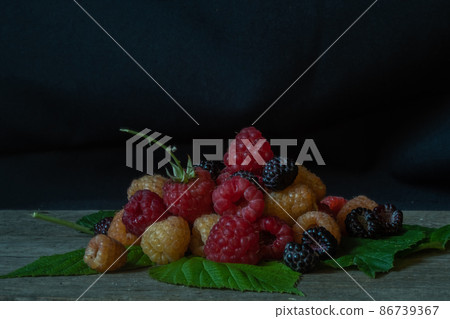 Different varieties of raspberries on a wooden table on a black 86739367