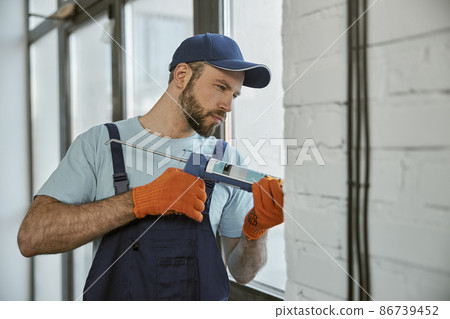 Bearded young man repairing window with special tool Bearded young man repairing window with special tool 86739452