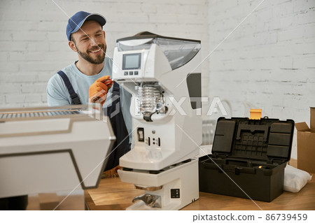 Cheerful repairman fixing coffee machine in cafe Cheerful repairman fixing coffee machine in cafe 86739459