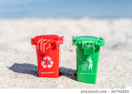 Different colored trash cans  red and green with paper, plastic, glass and organic waste suitable for recycling on sandy beach. Segregate waste, sorting garbage 86740889