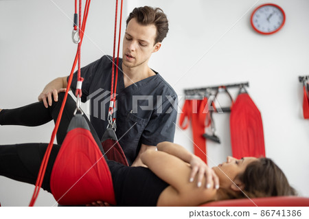 Rehabilitation specialist doing active treatment on suspension straps to a male patient Rehabilitation specialist doing active treatment on suspension straps to a male patient 86741386