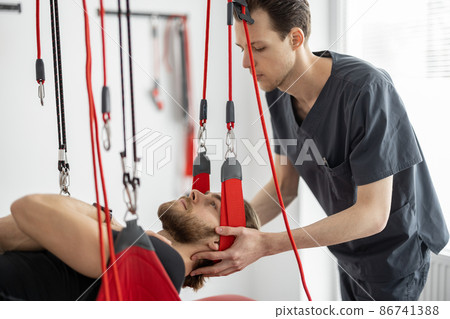 Rehabilitation specialist doing active treatment on suspension straps to a male patient Rehabilitation specialist doing active treatment on suspension straps to a male patient 86741388