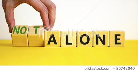 You are not alone symbol. Businessman turns wooden cubes and changes words alone to not alone. Beautiful yellow table white background, copy space. Business, support you are not alone concept. 86742040