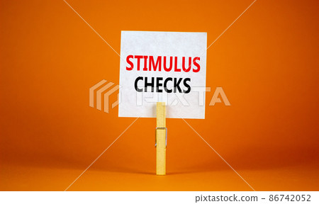 Stimulus checks symbol. White paper with words 'Stimulus checks', clip on wooden clothespin. Beautiful orange background. Business and Stimulus checks concept. Copy space. 86742052