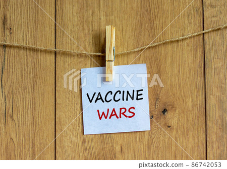 COVID-19 vaccine wars symbol. White paper with text 'vaccine wars', clip on wood clothespin. Beautiful wooden background. COVID-19 vaccine wars concept. 86742053