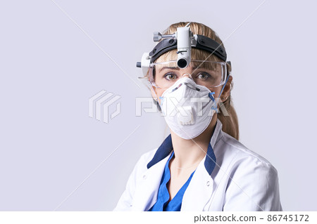 Confident ENT doctor wearing surgical headlight head light and protective glasses. Portrait of female otolaryngologist or head and neck surgeon on light grey background. 86745172