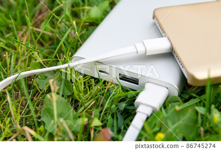Smartphone charging with powerbank on green lawn. Smartphone charging with powerbank on green lawn. 86745274