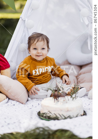 Baby boy looking on birthday cake while sitting in wigwam Baby boy looking on birthday cake while sitting in wigwam 86745304