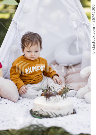 Baby boy looking on birthday cake while sitting in wigwam Baby boy looking on birthday cake while sitting in wigwam 86745306