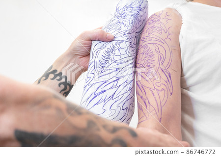 Skilled Tattoo artist putting a sketch on the arm of a man. Skilled Tattoo artist putting a sketch on the arm of a man. 86746772