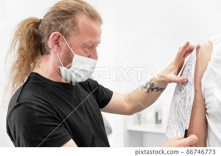 Skilled Tattoo artist putting a sketch on the arm of a man. 86746773