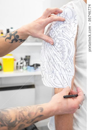 Skilled Tattoo artist putting a sketch on the arm of a man. Skilled Tattoo artist putting a sketch on the arm of a man. 86746774