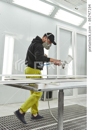 Man painting furniture details. Worker using spray gun. View of the paint shop of carpentry 86747194