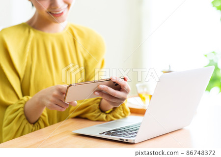A woman who uses a computer and a smartphone in the living room. A woman who uses a computer and a smartphone in the living room. 86748372