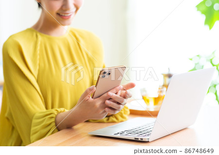 一個在客廳裡使用電腦和智能手機的女人。 一個在客廳裡使用電腦和智能手機的女人。 86748649