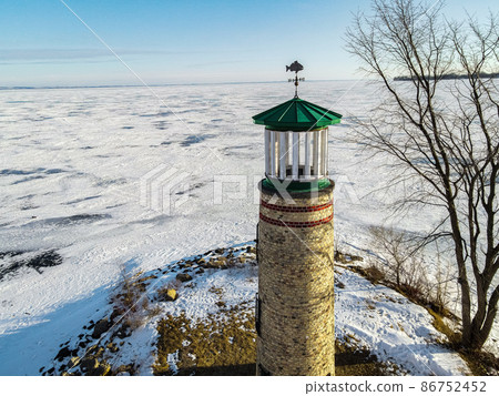 The land and water is frozen with snow coverings. This old light house at a park stands watch. 86752452