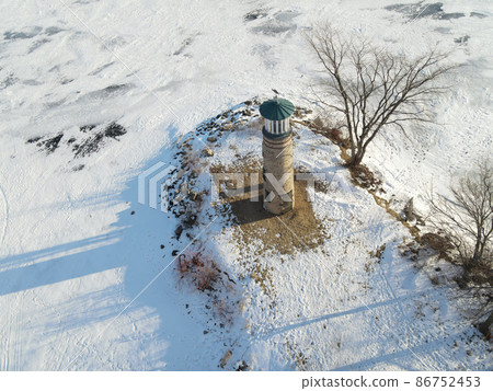 The land and water is frozen with snow coverings. This old light house at a park stands watch. 86752453