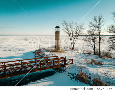The land and water is frozen with snow coverings. This old light house at a park stands watch. 86752456