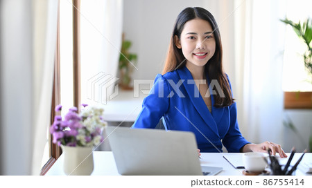Gorgeous businesswoman siting at comfortable workplace and smiling at camera. Gorgeous businesswoman siting at comfortable workplace and smiling at camera. 86755414
