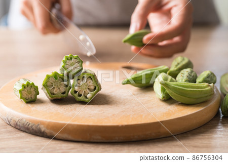 Hand holding knife and cutting green okra or ladies' fingers (Edible green seed pods) Hand holding knife and cutting green okra or ladies' fingers (Edible green seed pods) 86756304