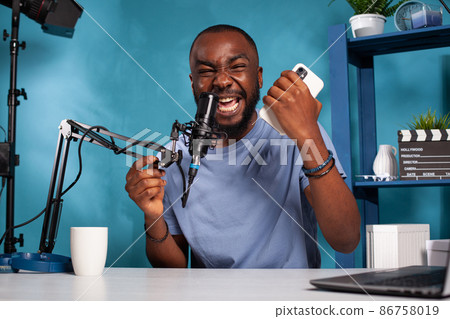 Influencer screaming after reading on smartphone insulting comments from online social media 86758019