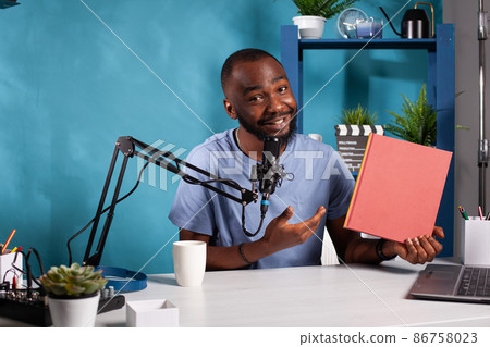 Smiling content creator reviewing red cover mockup book talking using professional microphone 86758023