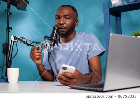 Portrait of african american vlogger holding boom arm microphone close to mouth answering messages 86758035