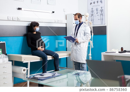 Specialist with face mask consulting pregnant woman in medical cabinet 86758360