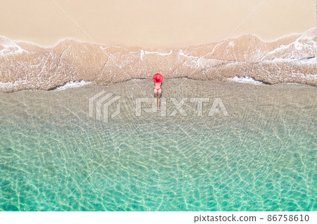 Top view. Young beautiful woman in a red hat and bikini lying and sunbathe in sea water on the sand beach. Drone, copter photo. Summer vacation. View from above. 86758610