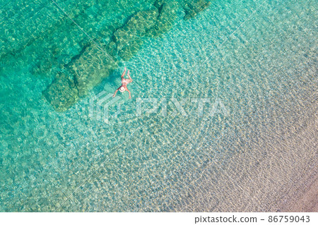 Top, aerial view. Young beautiful woman in a hat and white bikini swimming in sea water on the sand beach. Drone, copter photo. Summer vacation. View from above. Top, aerial view. Young beautiful woman in a hat and white bikini swimming in sea water on the sand beach. Drone, copter photo. Summer vacation. View from above. 86759043