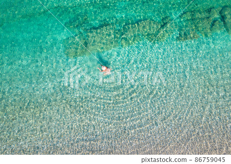 Top, aerial view. Young beautiful woman in a hat and white bikini swimming in sea water on the sand beach. Drone, copter photo. Summer vacation. View from above. Top, aerial view. Young beautiful woman in a hat and white bikini swimming in sea water on the sand beach. Drone, copter photo. Summer vacation. View from above. 86759045