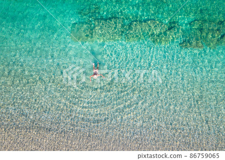 Top, aerial view. Young beautiful woman in a hat and white bikini swimming in sea water on the sand beach. Drone, copter photo. Summer vacation. View from above. Top, aerial view. Young beautiful woman in a hat and white bikini swimming in sea water on the sand beach. Drone, copter photo. Summer vacation. View from above. 86759065