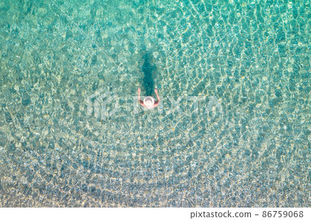 Top, aerial view. Young beautiful woman in a hat and white bikini swimming in sea water on the sand beach. Drone, copter photo. Summer vacation. View from above. Top, aerial view. Young beautiful woman in a hat and white bikini swimming in sea water on the sand beach. Drone, copter photo. Summer vacation. View from above. 86759068