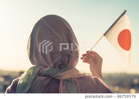 Muslim woman in scarf with Japanese flag of at sunset. Concept Muslim woman in scarf with Japanese flag of at sunset. Concept 86759579