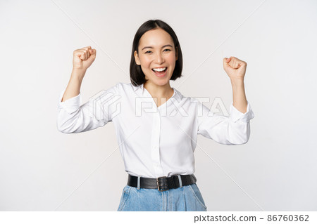Enthusiastic asian woman rejoicing, say yes, looking happy and celebrating victory, champion dance, fist pump gesture, standing over white background 86760362