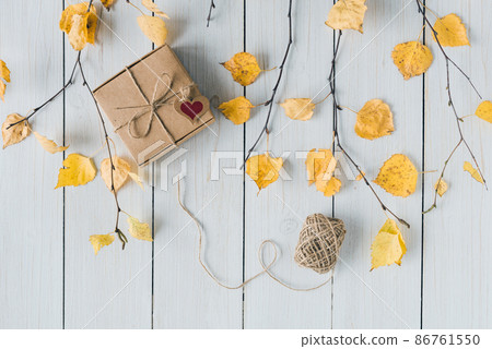 Woman packing gift in a box of kraft paper on white retro wood boards. leaves, birch branches. Thanksgiving. Autumn, fall concept. Flat lay, top view. 86761550