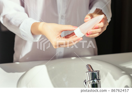 Woman applying cream after washing hands for protective and care dry skin near white sink in bathroom with sunlight from the window. 86762457