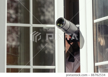 Private detective with spying zoom lens camera taking picture through open window. Closeup. concept 86762534
