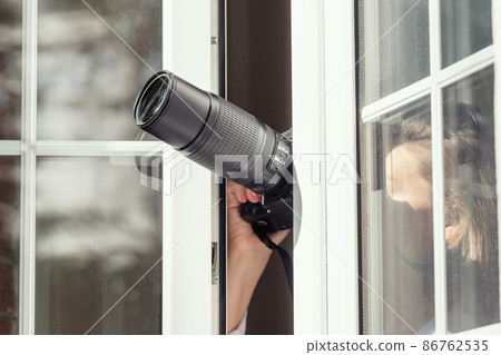 Private detective with spying zoom lens camera taking picture through open window. Closeup. concept 86762535