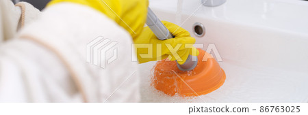 Person in yellow gloves is cleaning sink from blockage closeup Person in yellow gloves is cleaning sink from blockage closeup 86763025