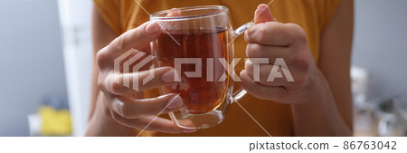 Woman holds transparent cup of hot tea in hands closeup Woman holds transparent cup of hot tea in hands closeup 86763042