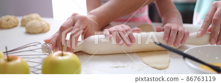 Adult and child roll out dough with rolling pin on table closeup 86763119