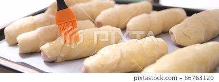 Female chef applies brush of egg yolk to croissants closeup Female chef applies brush of egg yolk to croissants closeup 86763120