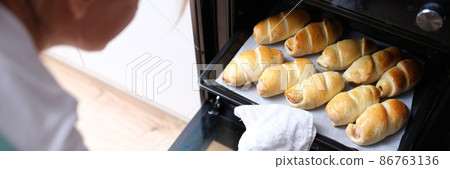 Woman takes out baking sheet of cooked croissants from oven closeup Woman takes out baking sheet of cooked croissants from oven closeup 86763136