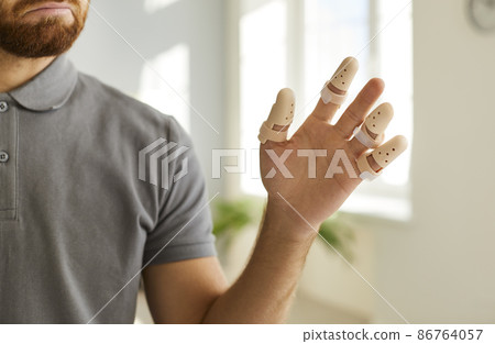 Close up of man's hand wearing adjustable splint braces on injured or broken fingers. Cropped image of man who is forced to wear orthopedic devices to protect against pain or fracture of finger joint. 86764057