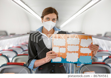 Female flight attendant in face mask holding instruction booklet Female flight attendant in face mask holding instruction booklet 86764561